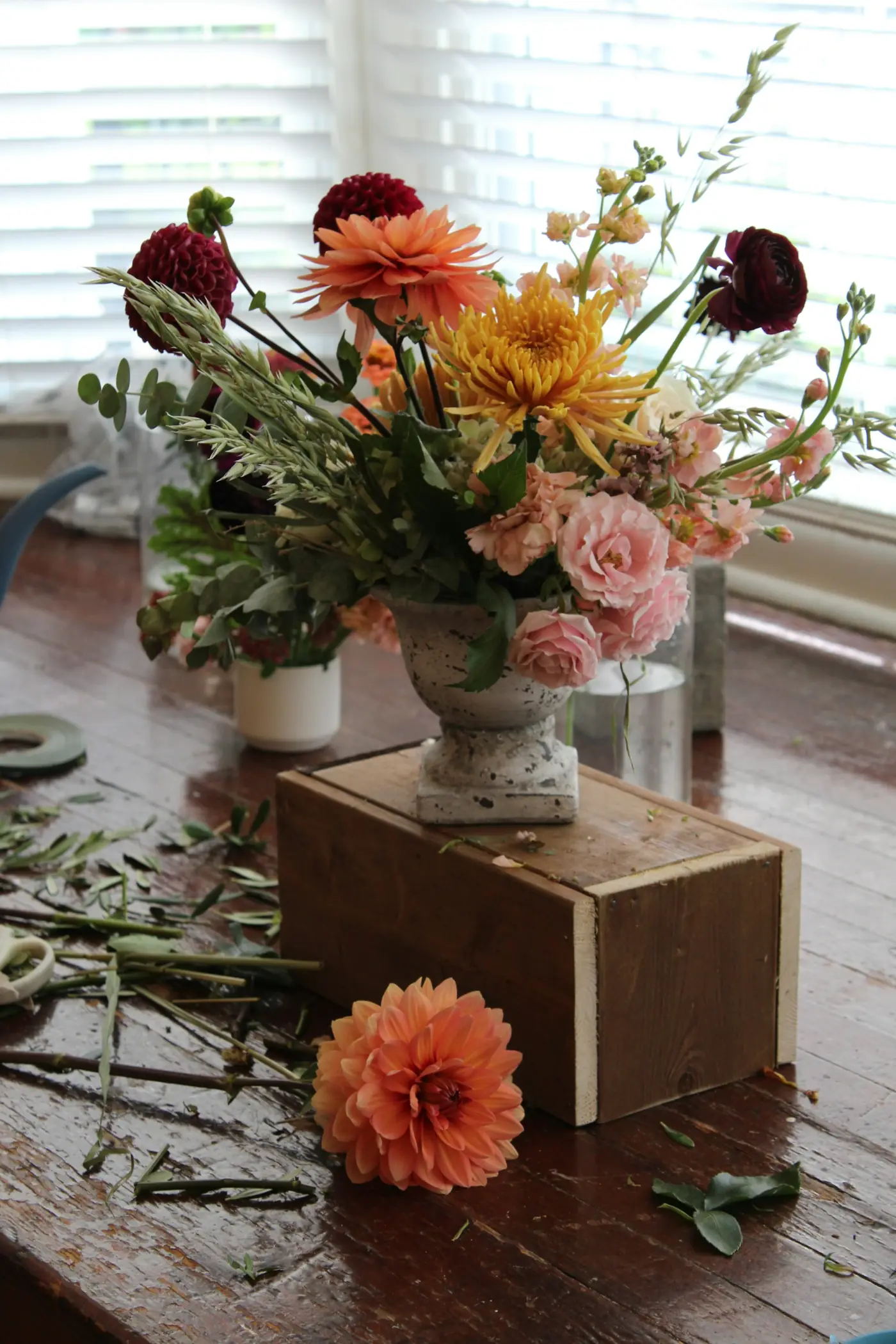 A complete wedding flower arrangement of dahlias, mums, garden roses, and greenery on a styled tabletop.